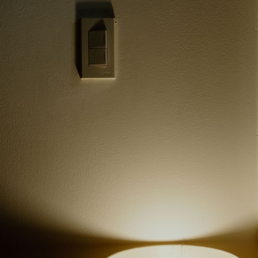 Abajur aceso iluminando a parede onde está um interruptor